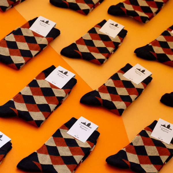 Calcetines de algodón con motivo tejido inspirado en el pavimento de la Catedral de Segovia, presentados en un patrón repetitivo sobre un fondo naranja, colección Pavimentos