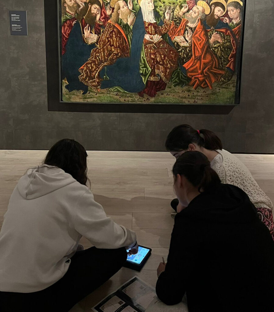 Jóvenes participando en un taller interactivo con tablet frente a una obra de arte en el Palacio Episcopal de Segovia.