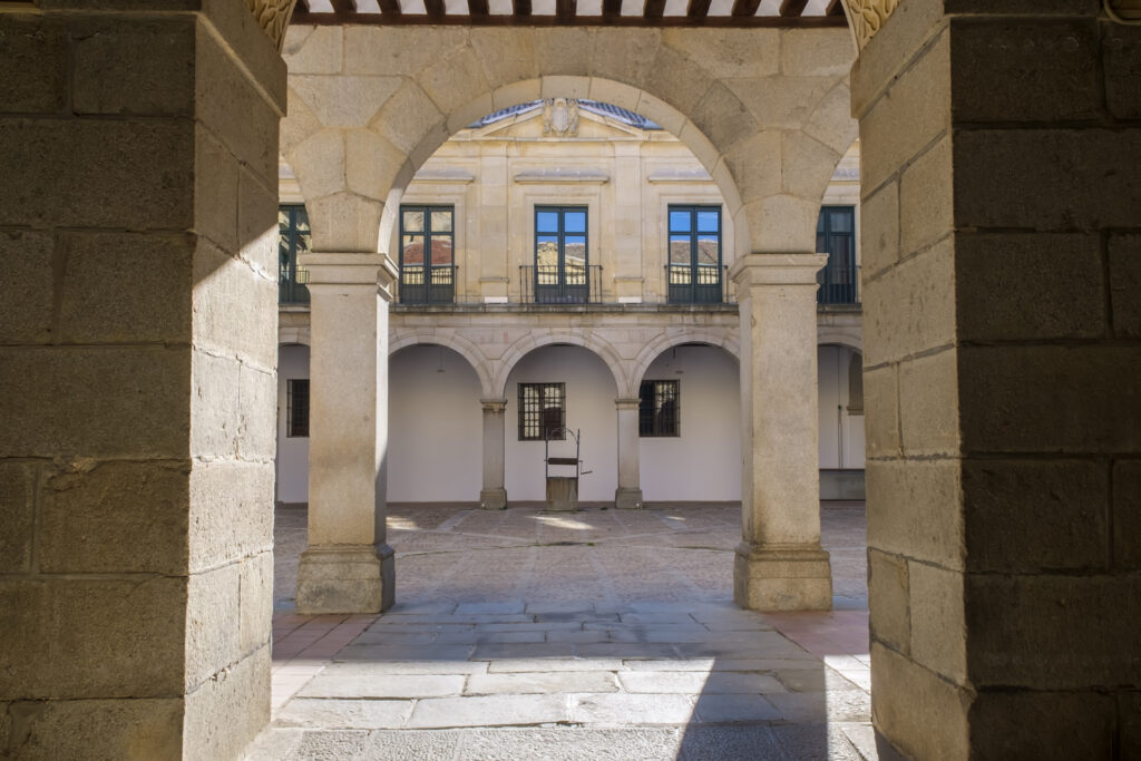 Vista desde la entrada del patio del Palacio Episcopal de Segovia, con columnas de piedra y arcos que enmarcan el pozo central.