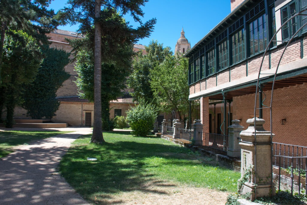 Jardín del Palacio Episcopal de Segovia, con estructura de hierro y granito, rodeado de árboles y plantas.