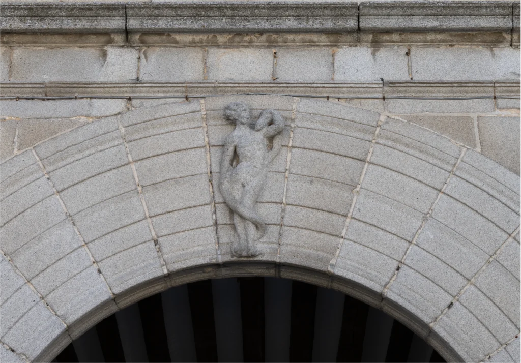 Primer plano del arco del Palacio Episcopal de Segovia con esculturas decorativas y un escudo en la parte superior.